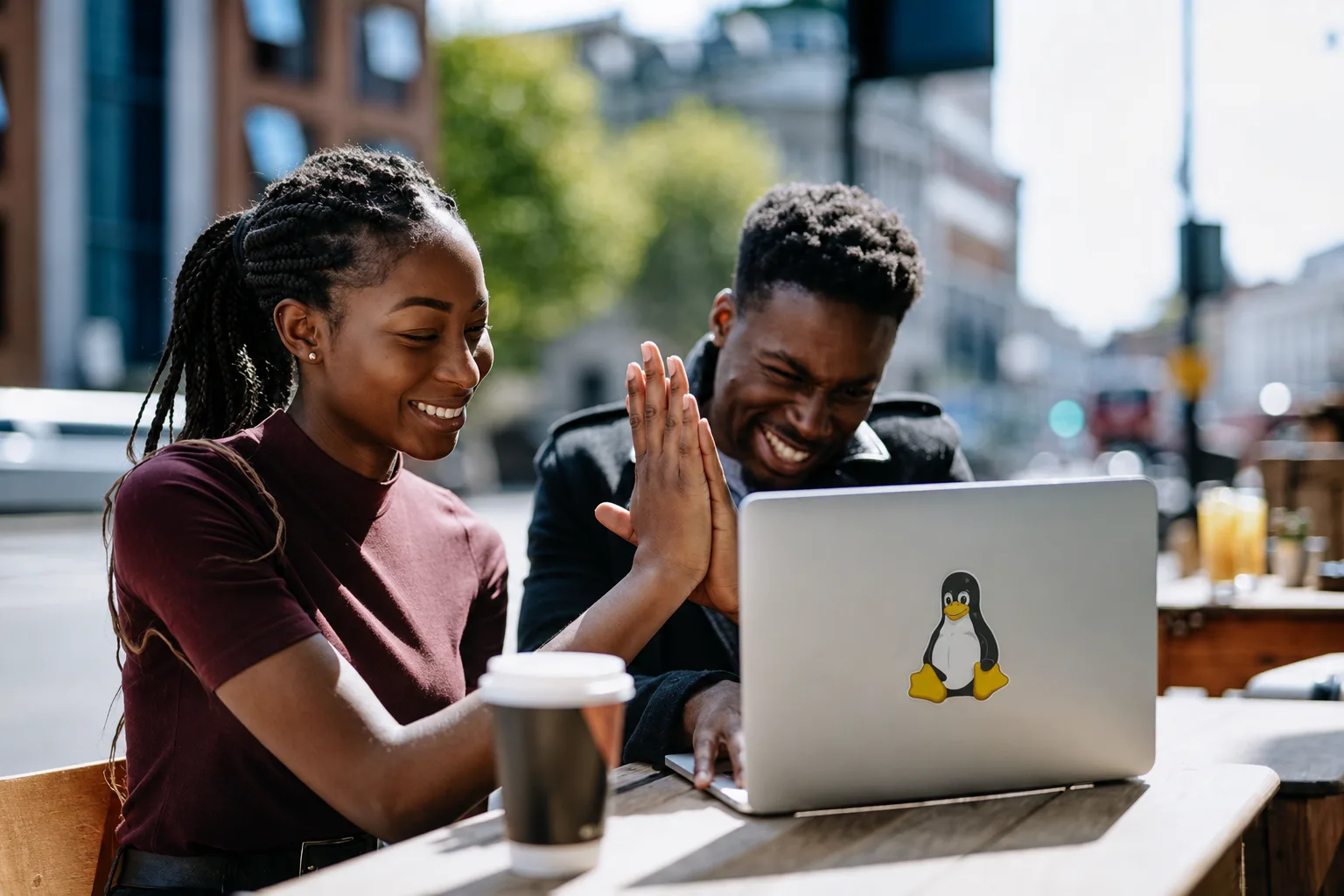 Two young founders high-five in front of a laptop at an outdoor café table